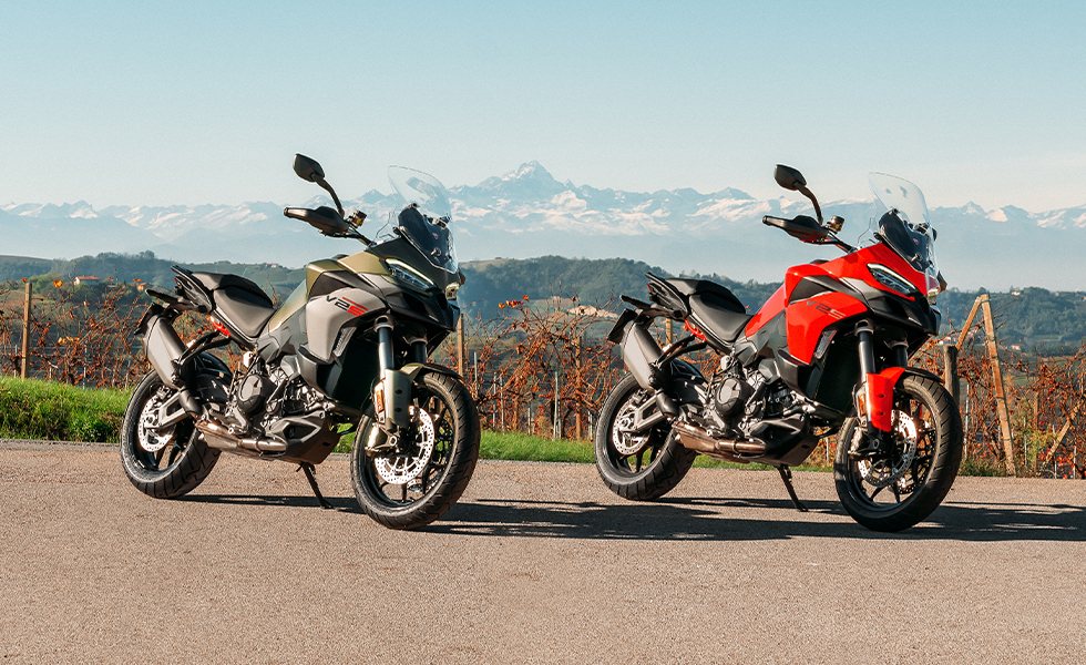 Two Ducati Multistrada V2 S, olive and red, parked above a vineyard with the Alps behind